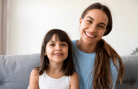 A smiling mother and daughter sitting together on a couch, looking happy and relaxed.